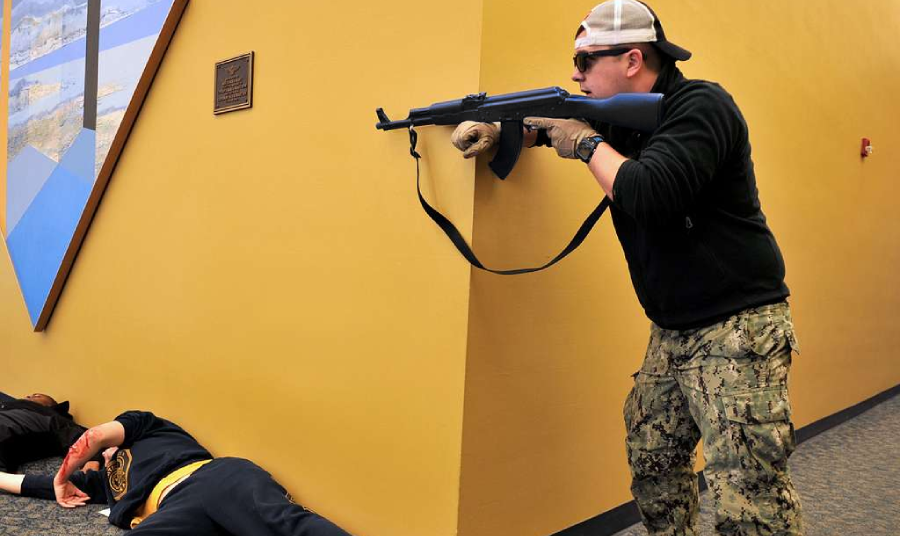 A tactical simulation scene shows a person holding a rifle while taking cover behind a wall.