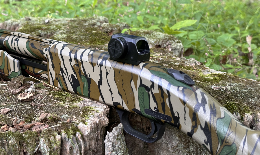 A close-up image of a camouflaged shotgun resting on a tree stump in a woodland setting.
